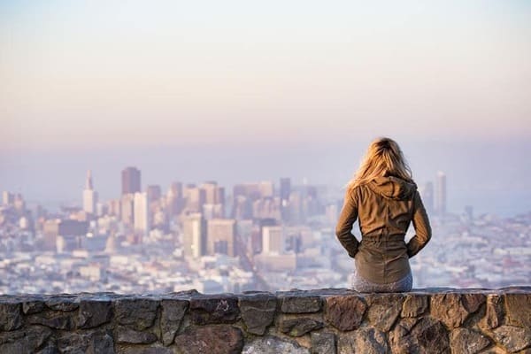 Mujer sentada en un muro mirando una ciudad de fondo